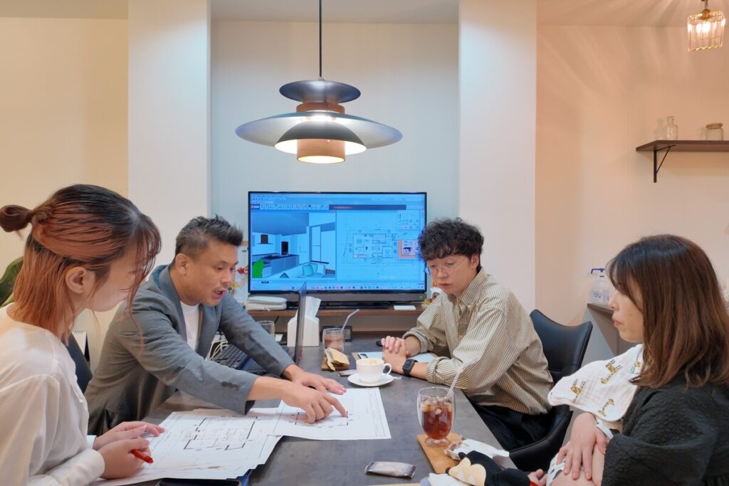 住宅の設計図を囲み、リビングダイニングのテーブルで複数人が打ち合わせを行っている計画風景