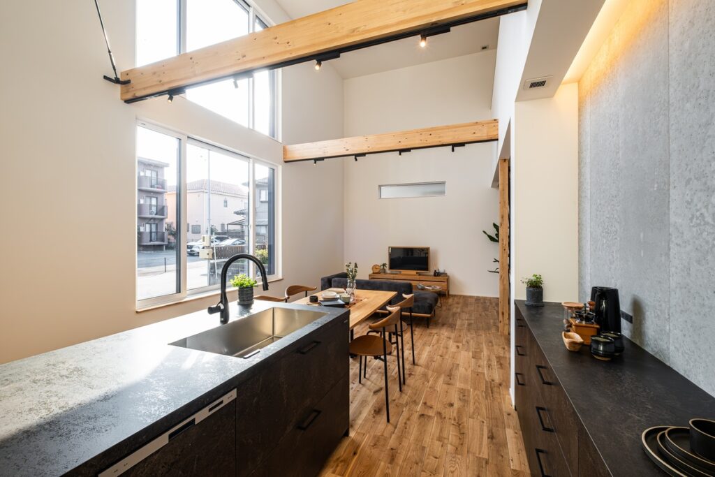 吹き抜け天井と大きな窓から自然光が入る、木梁とアイランドキッチンを備えた開放的なLDK空間
