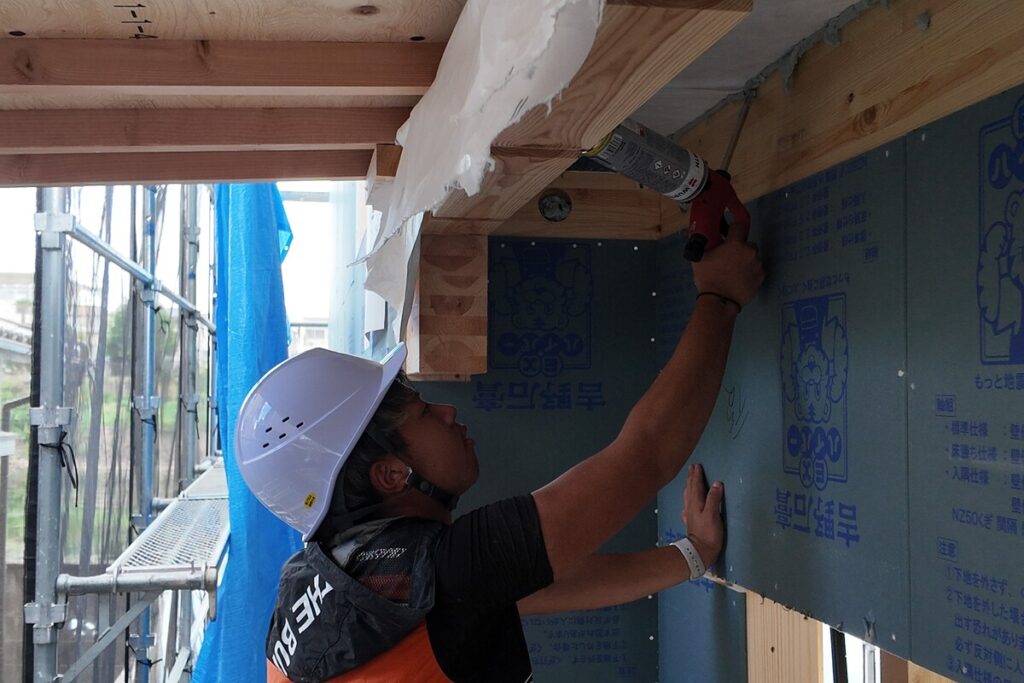 断熱材を吹き付け施工している職人の様子と、構造材が見える建築現場