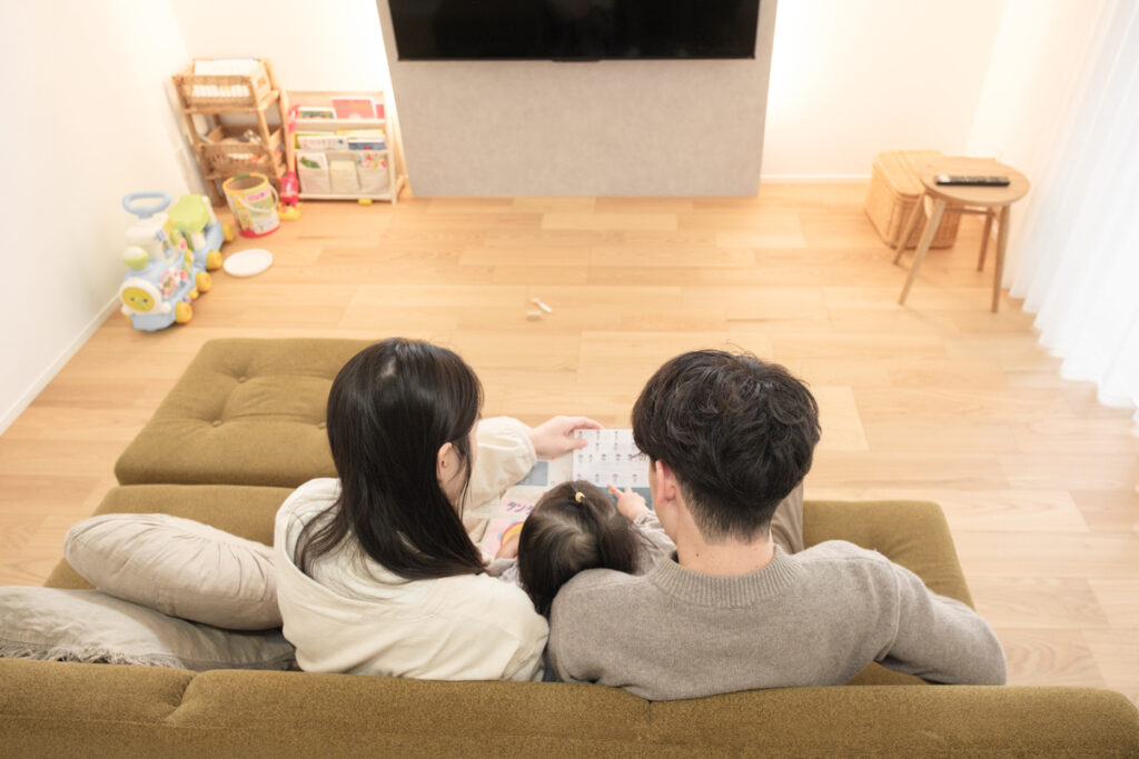 リビングのソファに座り、親子で絵本を一緒に読んでいる背面からの暮らしの様子