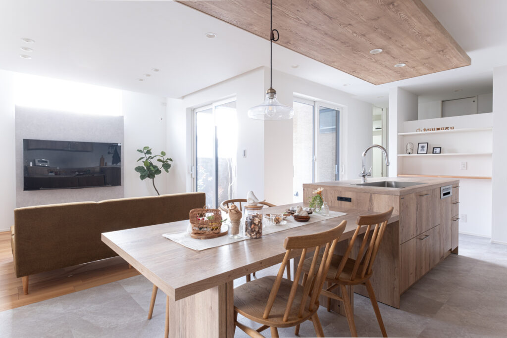 木目調のアイランドキッチンとダイニングテーブルが一体となった、開放的で明るいナチュラルモダンなLDKの内観。