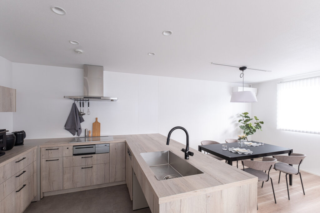 木目調の面材が美しいL字型キッチンと、黒の家具が調和する開放的なダイニング。天井のダウンライトがスッキリとした印象。