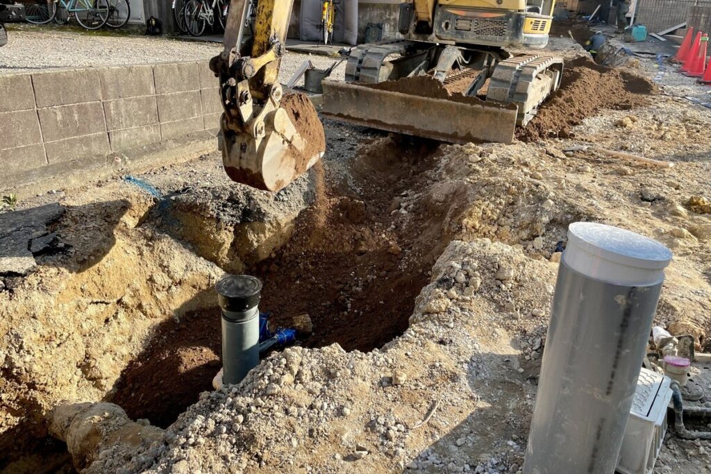 土地のインフラ整備のため、重機で地面を掘削し、新しい給排水管を埋設する水道引き込み工事の様子。