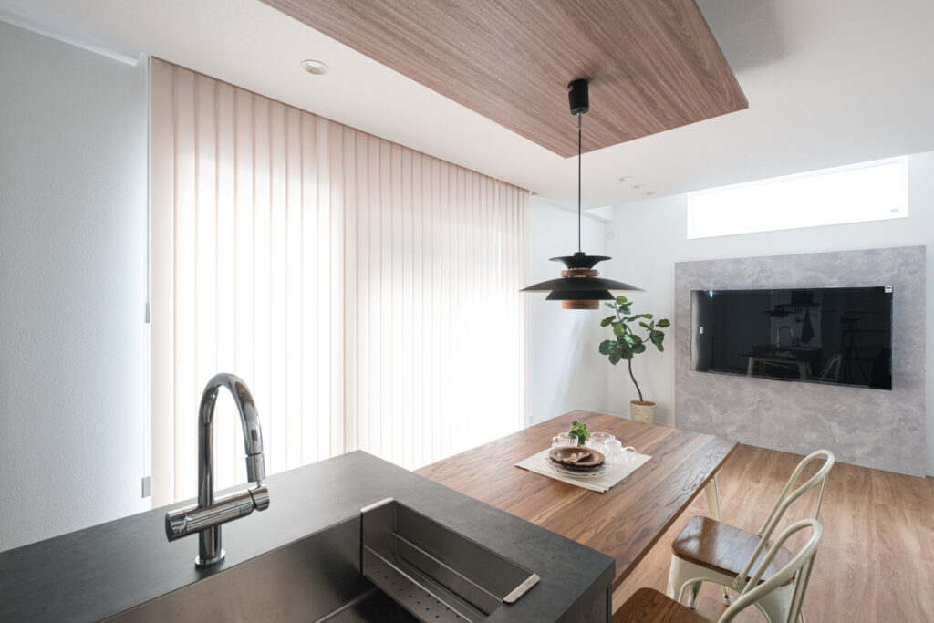 洗練されたダークグレーのキッチンカウンターと、木目の天井パネルが調和する、モダンで開放的なダイニング・リビングのインテリア。