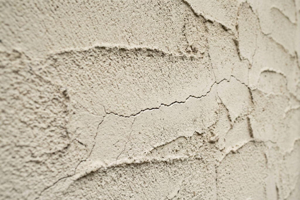 塗り壁の外壁に発生した細かなひび割れ（クラック）の近接。住宅の美観と耐久性を維持するために見逃せない、メンテナンス時期の重要なサイン。