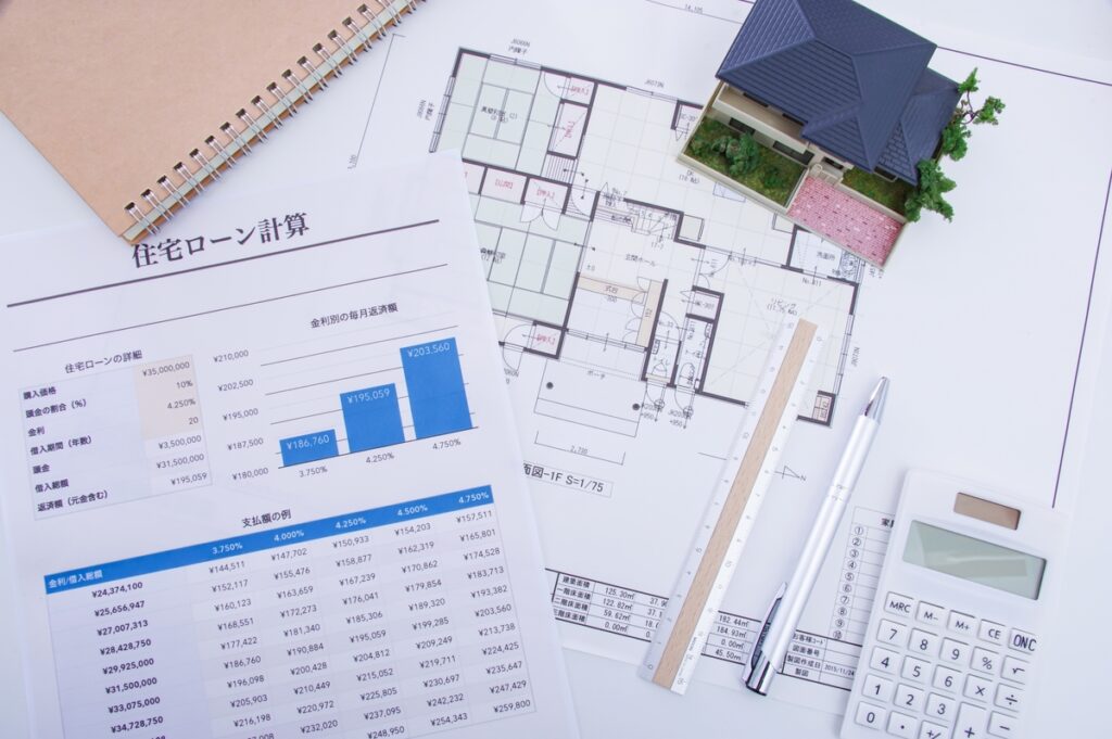 設計図や住宅模型、計算機とともに広げられた住宅ローン計算書。間取りの検討と並行して進める、家づくりのための具体的な資金計画の様子。