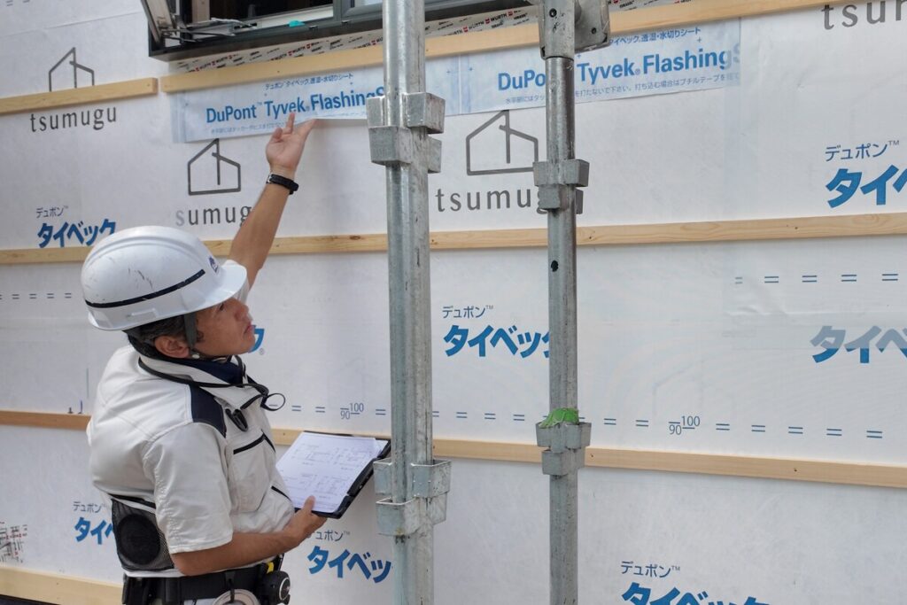 外壁の防水透湿シートの重なりや施工精度を、図面を確認しながら現場で入念にチェックする現場監督。