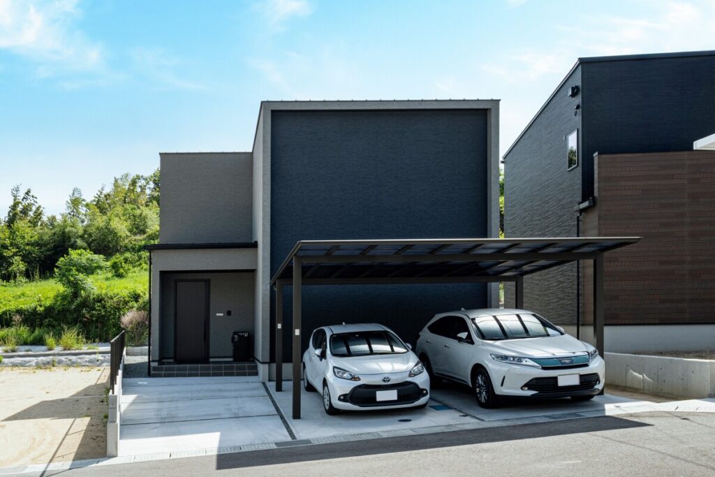 グレーと黒のバイカラーが印象的なスクエア住宅に、2台並列駐車が可能な広々としたカーポートが設置された外構デザイン。