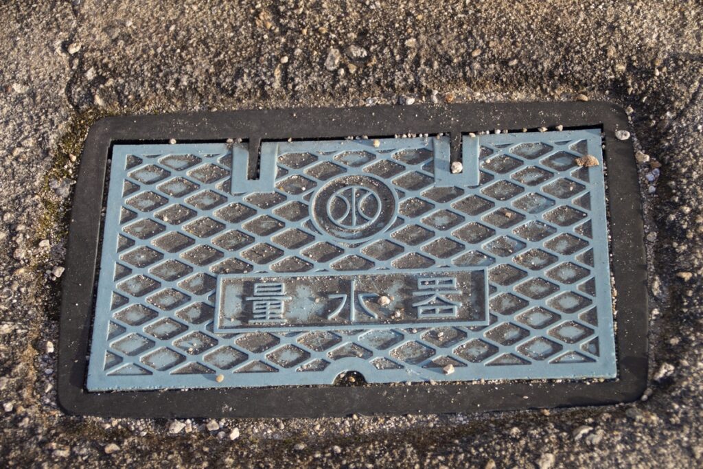 敷地内の地面に設置された「量水器」と書かれた水道メーターボックスの蓋。土地の水道引き込み状況を確認する際の重要な目印。