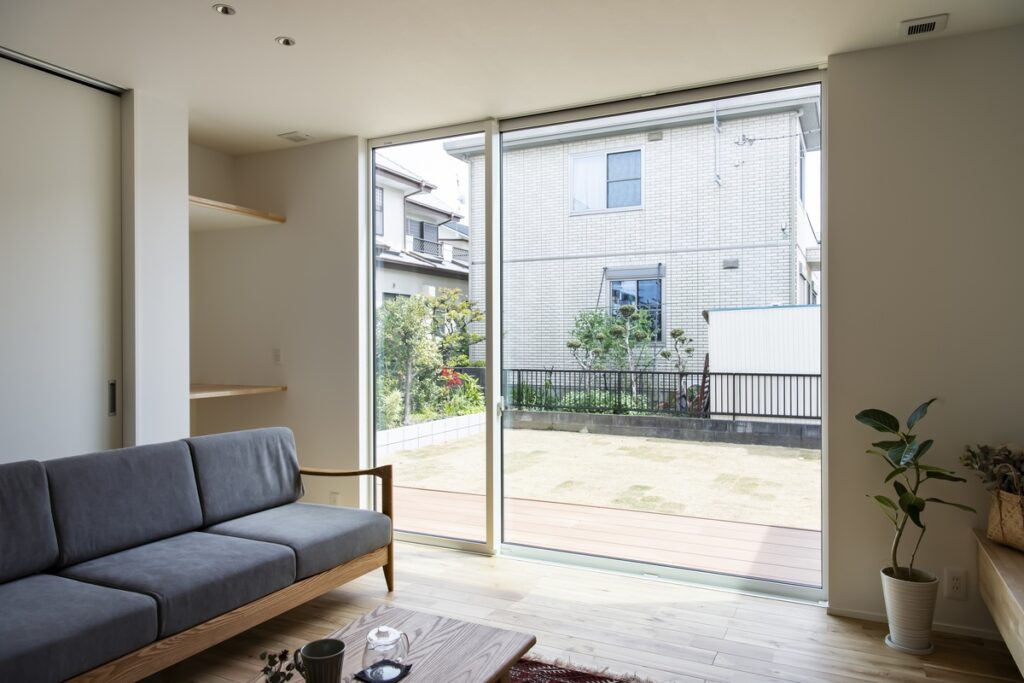 明るい光が差し込むリビングルーム。大きな掃き出し窓からはウッドデッキと芝生の庭が広がり、室内の無垢フローリングと外の景色が繋がるような開放感のある住空間。