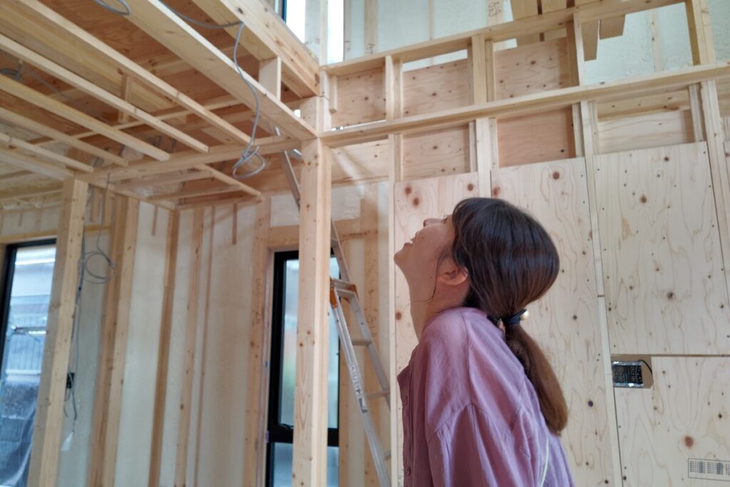 木造住宅の構造現場で、天井を見上げて施工の進捗を興味深く確認している施主の様子。