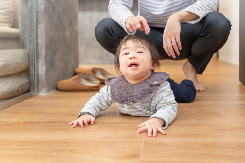 木の温もりが感じられる無垢フローリングの上で、のびのびとハイハイをする赤ちゃんと見守る父親の日常風景。