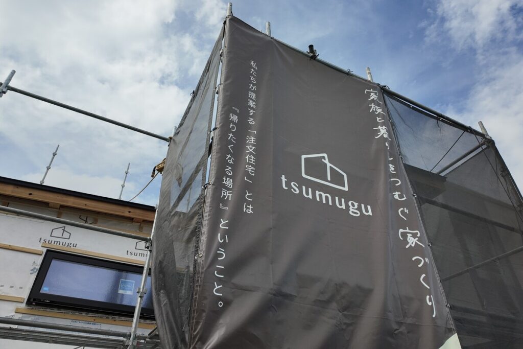 建設現場の足場に掲げられた「tsumugu」のブランドロゴ入り養生幕。丁寧な家づくりと、近隣への配慮を欠かさない現場管理を象徴する。