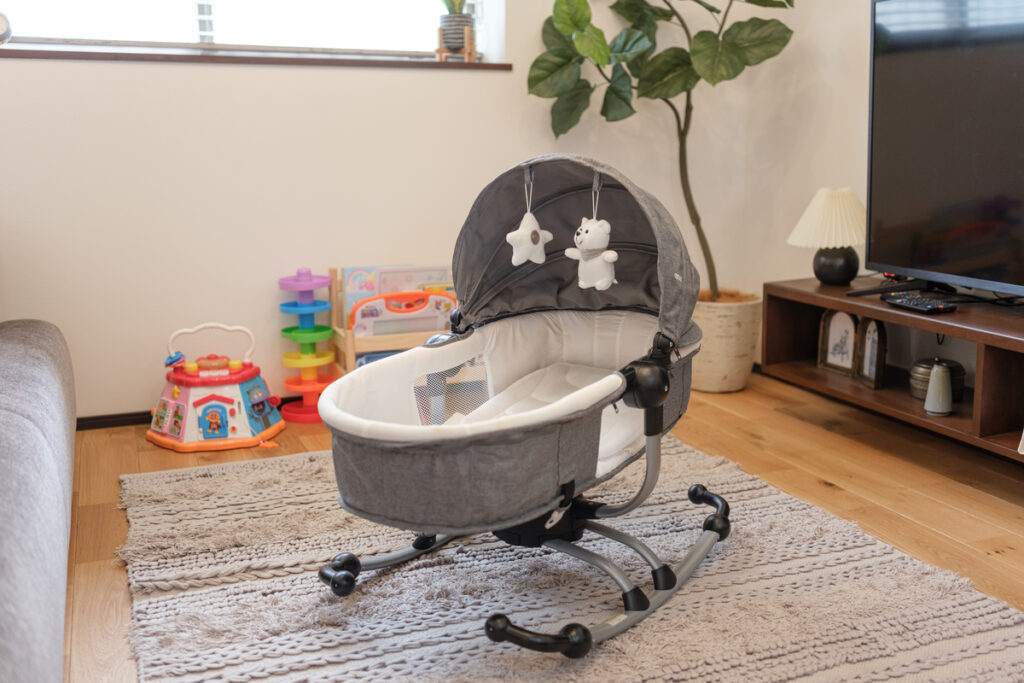 リビングのラグの上に置かれたおもちゃ付きのベビーバウンサーと、その周辺に広がる子育て世代のリアルな暮らし。