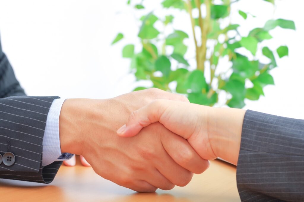 土地の売買契約や建築請負契約の成立を象徴する、担当者と施主が交わす信頼の握手のクローズアップ。