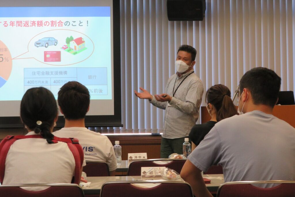 スクリーンに投影されたグラフを用いて、住宅ローンの仕組みや無理のない返済計画について熱心にレクチャーする家づくり勉強会。